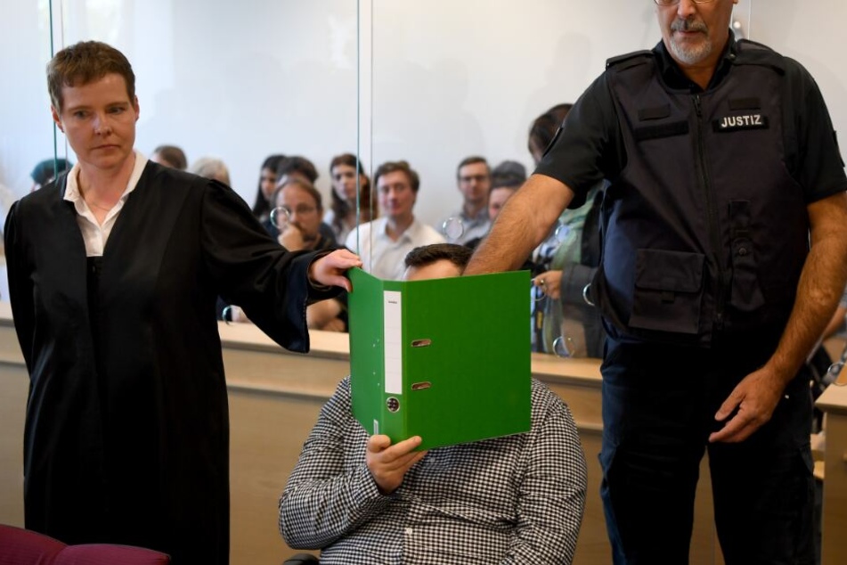 Mit verdecktem Gesicht sitzt der Angeklagte im Gerichtssaal.