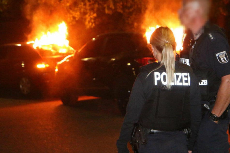 Polizisten stehen vor den brennenden Autos.