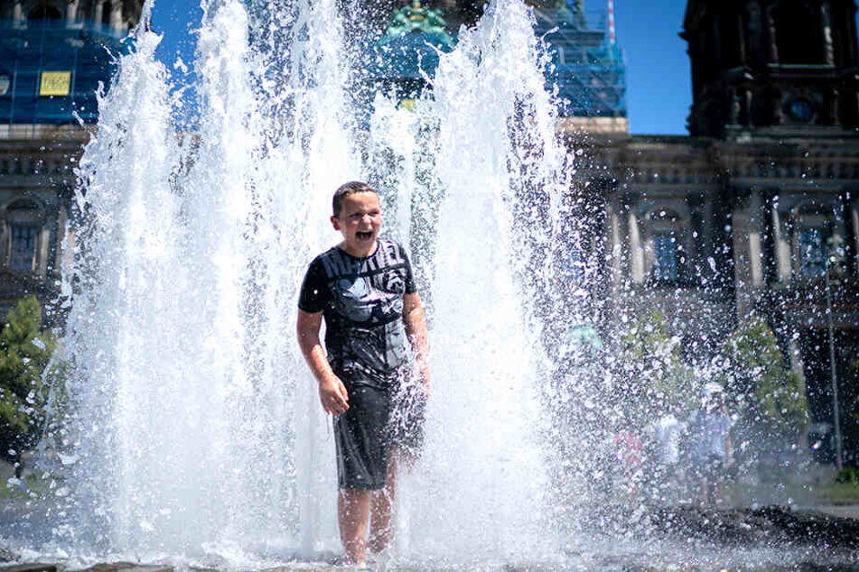 Abkühlung tut gut. Ein kleiner Junge genießt das kühle Nass in einem Springbrunnen.