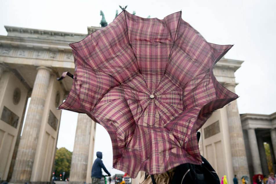 Eine Passantin kämpft mit ihrem Regenschirm vor dem Brandenburger Tor gegen den Wind.