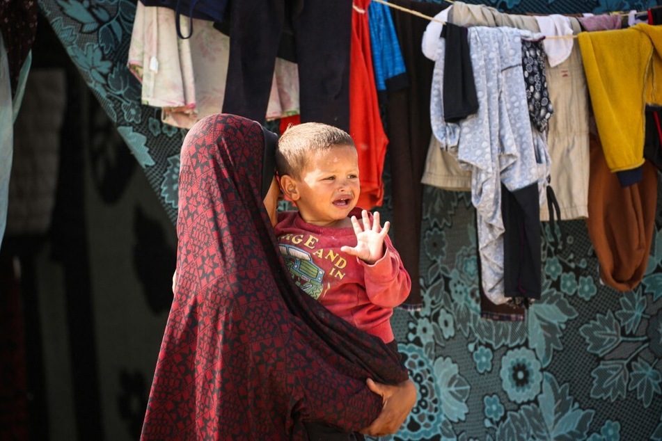 A displaced Palestinian woman carries her son at a temporary camp in Rafah on May 17, 2024.
