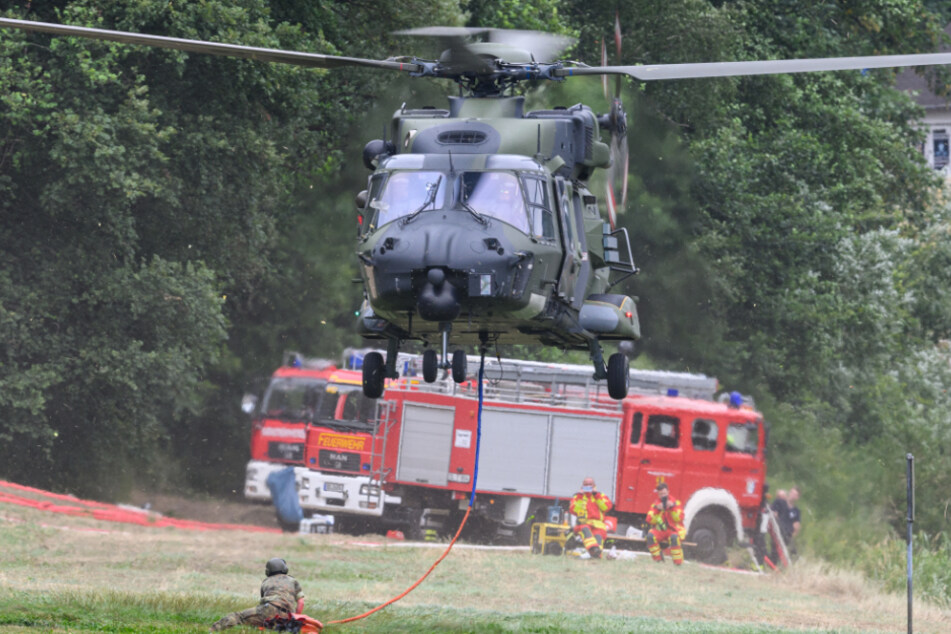 Ein Helikopter der Bundeswehr startet mit einem Löschwasser-Außenlastbehälter am Ufer der Elbe.