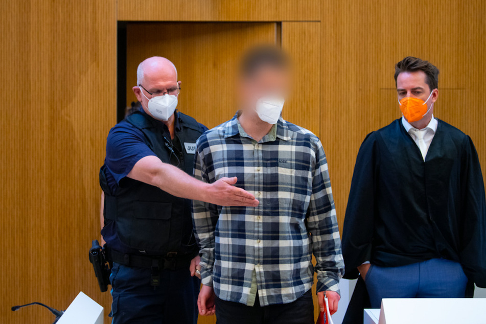Einer von zwei wegen Mordes angeklagten Männer (M.) wird vor Beginn der Verhandlung in den Sitzungssaal geführt. Rechts steht sein Anwalt Alexander Stevens.
