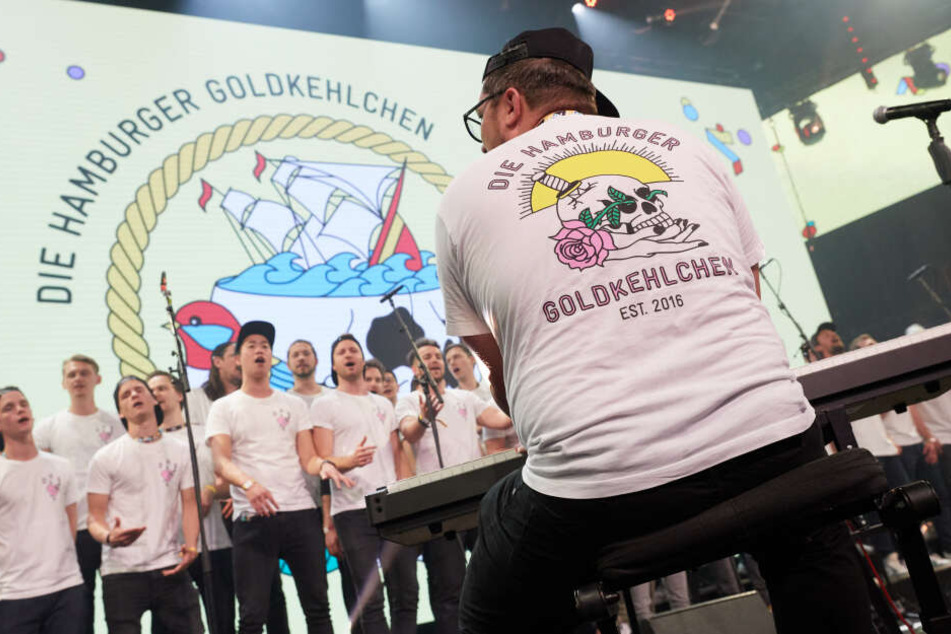 Der Männerchor Hamburger Goldkehlchen tritt auf einer Bühne auf.