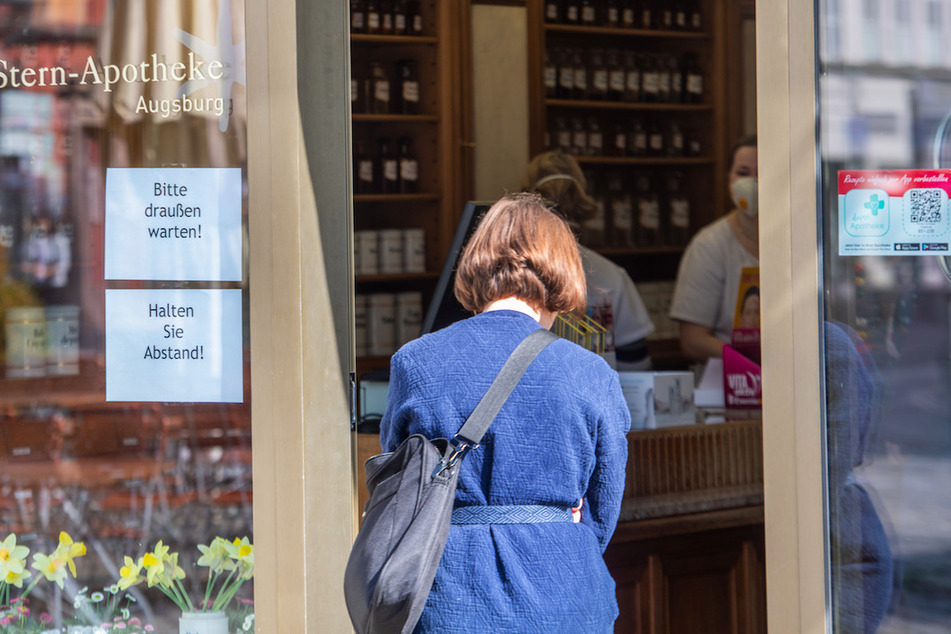 Vor der Tür einer Apotheke wartet eine Frau. Die Apotheke darf nur noch einzeln betreten werden.