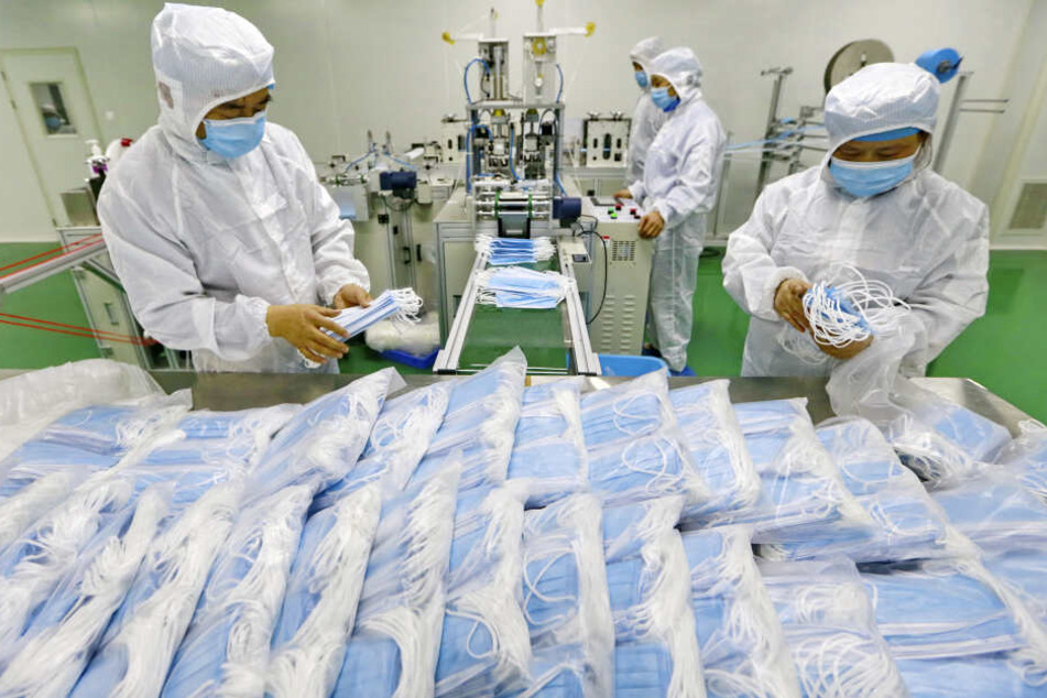 Arbeiter in einer Fabrik packen Schutzmasken ein.