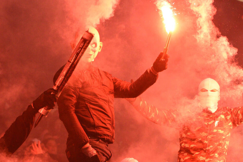 Mit Masken und vermummt halten Fans Pyro-Technik hoch.