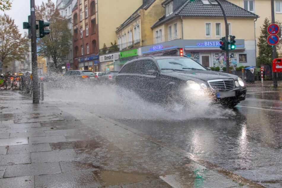 Ein Auto fährt durch eine große Pfütze und spritzt das Wasser auf.