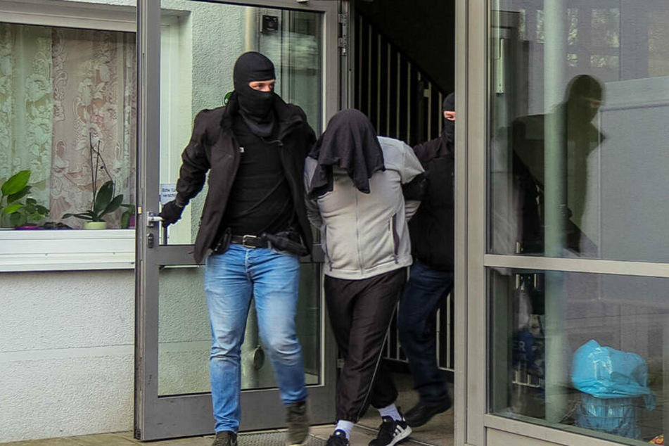 Der Tatverdächtige wird von zwei vermummten Beamten aus dem Haus geführt. (Archivbild)