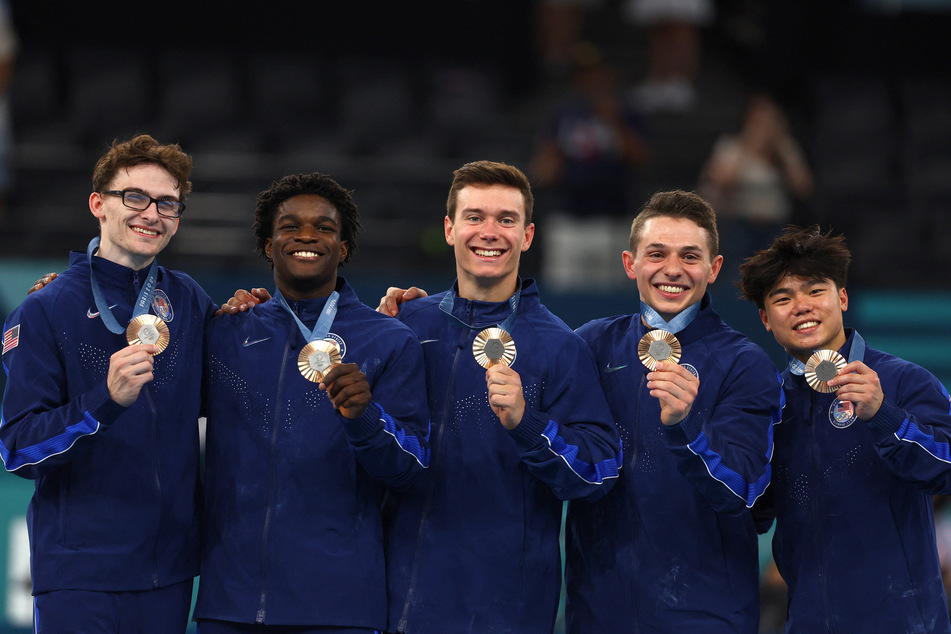 From l. to r.: Bronze medalists Stephen Nedoroscik, Frederick Richard, Brody Malone, Paul Juda, and Asher Hong of Team USA celebrate on the podium at the Paris Olympics.