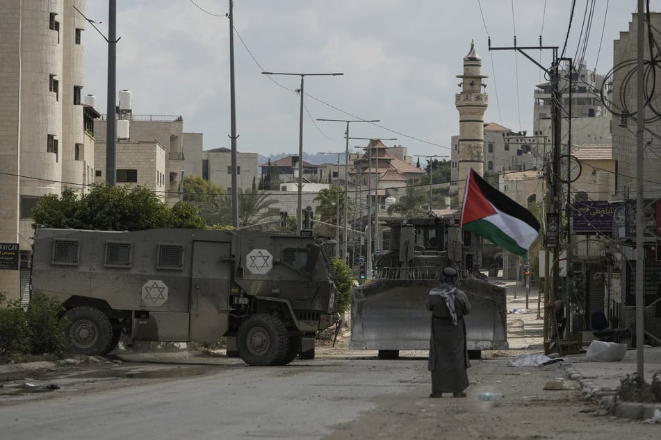 Der palästinensische Aktivist Khairi Hanoon schwenkt die palästinensische Flagge, als ein Konvoi gepanzerter israelischer Militärfahrzeuge während einer Razzia der Armee in Tulkarem, Westjordanland vorbeifährt. (Archivbild)