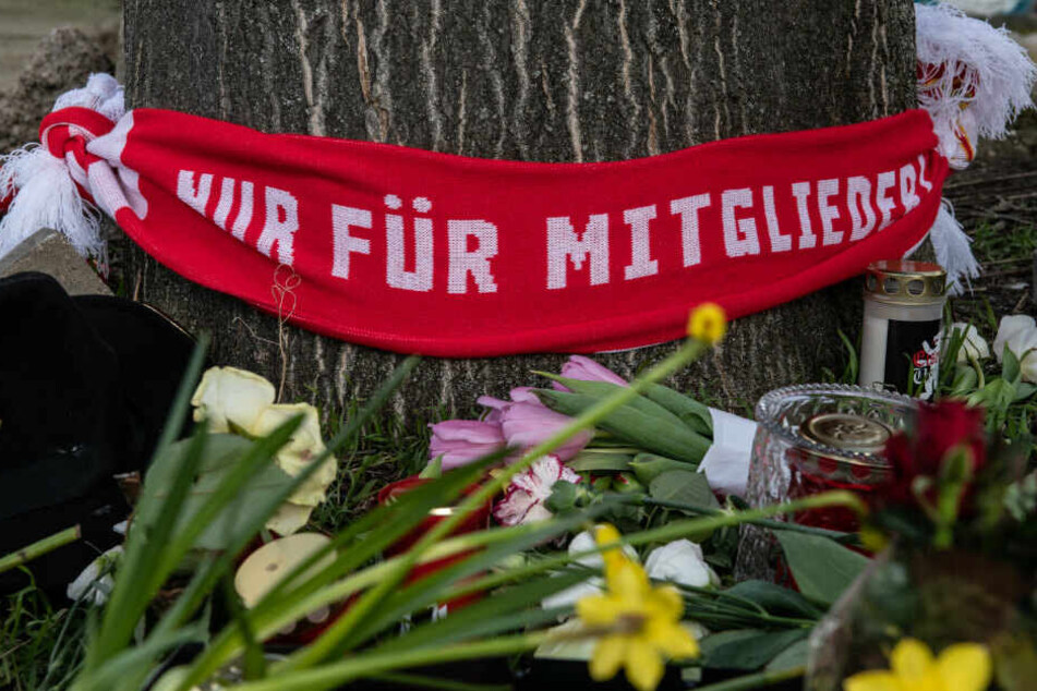 Blumen und Kerzen sowie ein Fan-Schal vom 1. FC Union haben Menschen auf einem Parkplatz an der Stahlheimer Straße abgelegt.