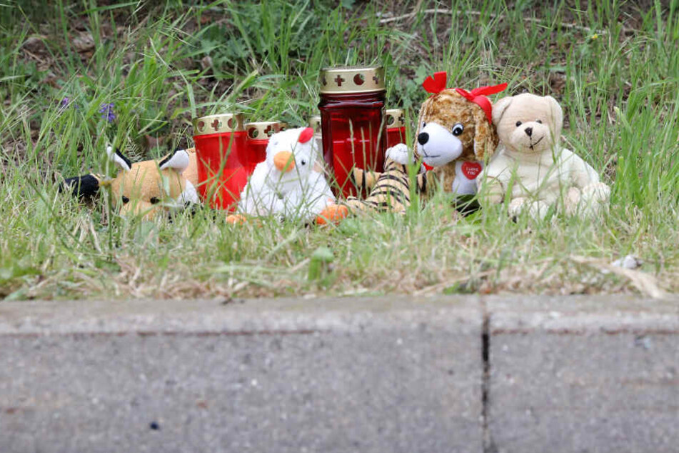 Blumen, Kerzen und Plüschtiere stehen an einer Stelle am Straßenrand im Stadtteil Lichtenhagen.