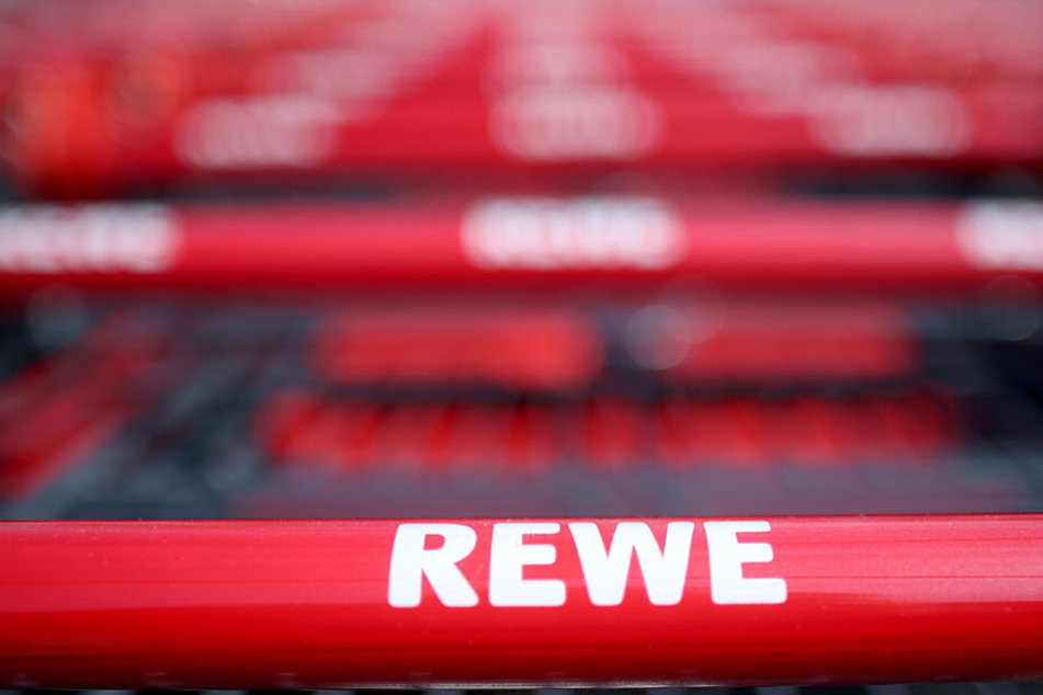Einkaufswagen stehen vor einem Rewe Supermarkt. (Symbolbild)