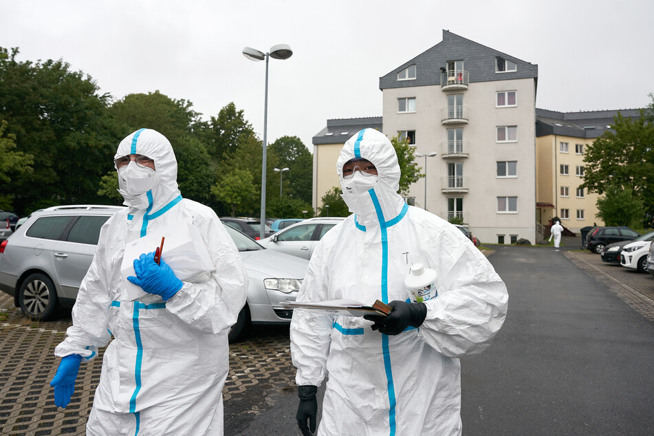 Einsatzkräfte in Schutzkleidung stehen vor einem der drei betroffenen Studentenwohnheime.