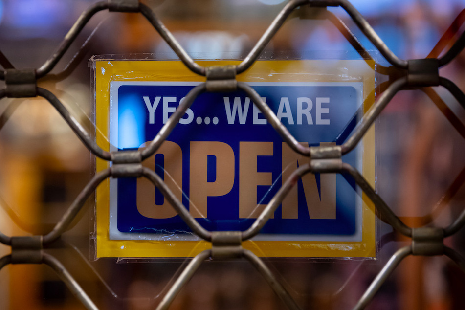 Ein Schild mit der Aufschrift "Yes...we are Open" ist an einem geschlossenen Geschäft in München zu sehen.