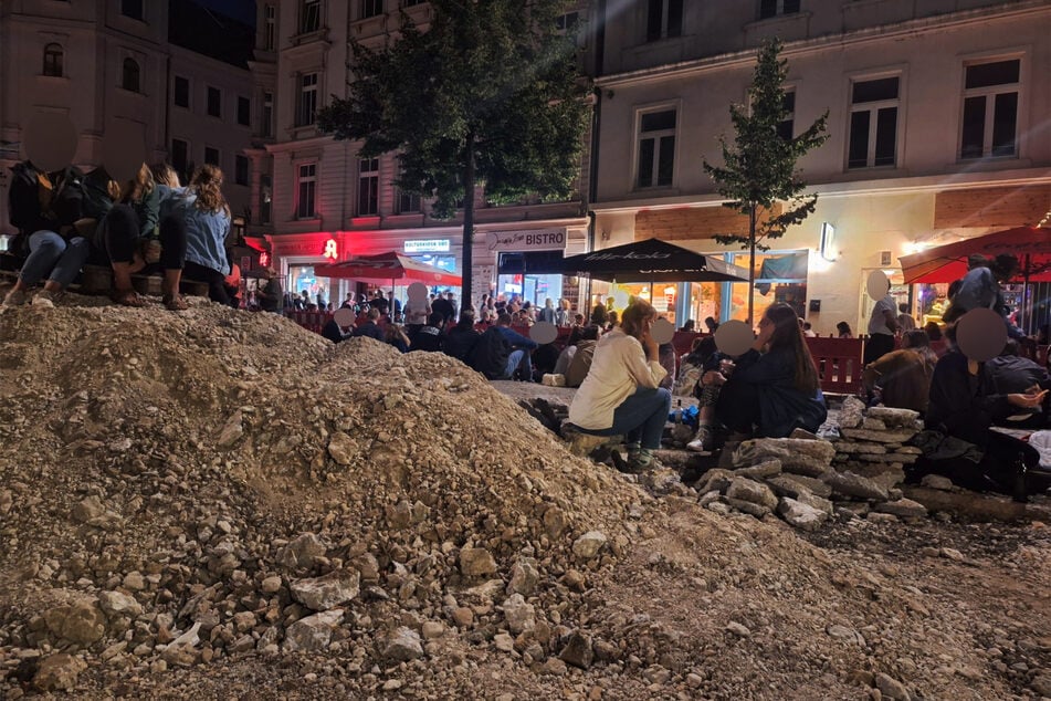 Die Menschen sitzen abends auf aufgeschütteten Sandbergen und Steinplatten.