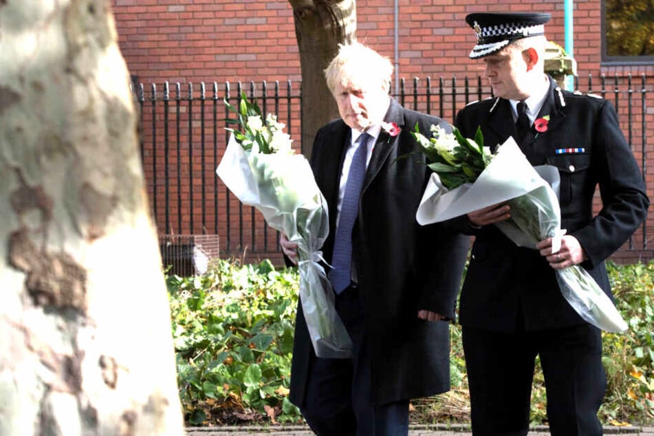 Boris Johnson (l), Premierminister von Großbritannien, und Ben-Julian Harrington, Polizeipräsident von Essex, tragen Sträuße mit weißen Blumen in den Händen