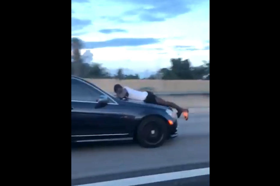 Der Mann liegt bei voller Geschwindigkeit auf der Motorhaube.