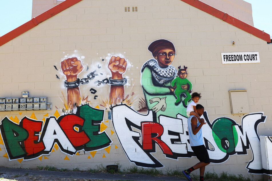 A man carrying a child walks past a mural in Cape Town, South Africa, symbolizing freedom and peace in support of Palestinians in Gaza.