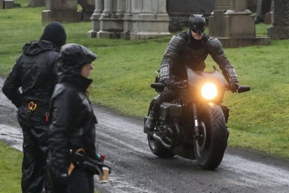 Ein Mann in Batman-Kostüm fährt während der Dreharbeiten zu "The Batman" auf einem Motorrad durch den Friedhof Glasgow Necropolis.