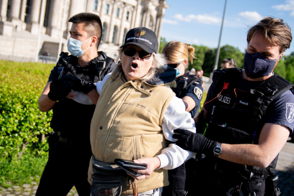 Eine Teilnehmerin wird von Polizeibeamten vor dem Reichstagsgebäude am Rande einer Demonstration gegen eine Impfpflicht abgeführt.