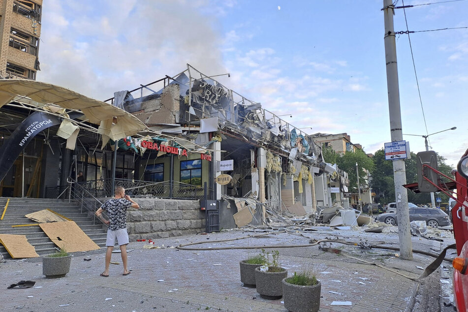 Hier steht ein Mann auf der Straße vor einem Geschäft und dem Restaurant RIA Pizza, das durch einen russischen Angriff zerstört wurde.