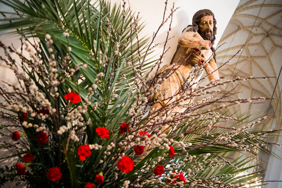Eine Jesusfigur ist beim Palmsonntags-Gottesdienst hinter einem Gesteck aus Palmwedeln und Weidenkätzchen in der Frauenkirche in München zu sehen.