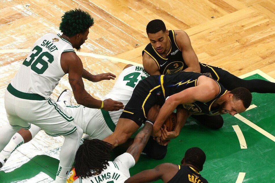 Stephen Curry and Jordan Poole of the Golden State Warriors compete for a loose ball against Al Horford of the Boston Celtics in the fourth quarter during Game Three of the 2022 NBA Finals.