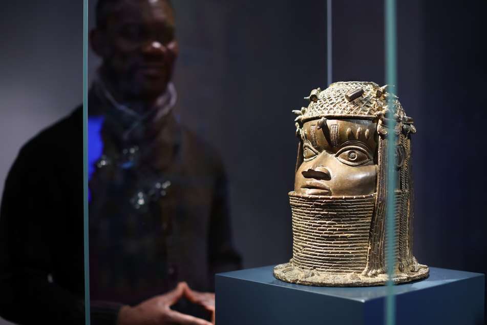 Der nigerianische Künstler Enotie Paul Ogbebor steht neben einer Benin-Bronze im Grassi Museum für Völkerkunde in Leipzig.