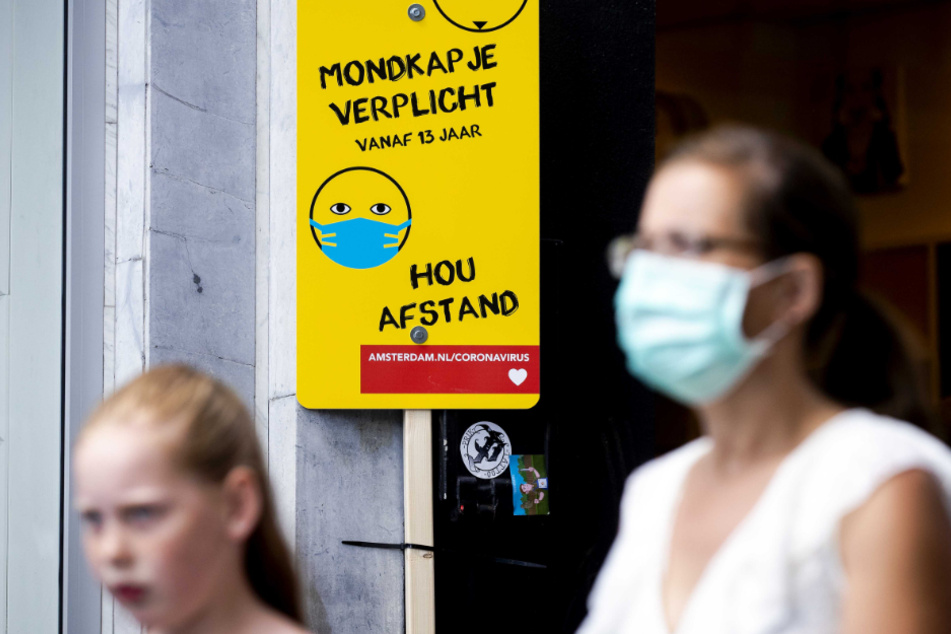 Amsterdam: Eine Frau mit Mundschutz geht an einem Schild mit Informationen über die Maskenpflicht vorbei.