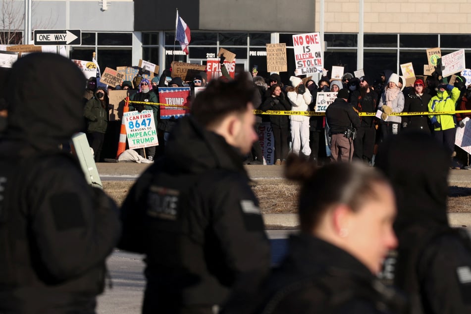Demonstrators hold signs outside the venue where President Donald Trump delivers a speech in Clive, Iowa, on January 27, 2026.