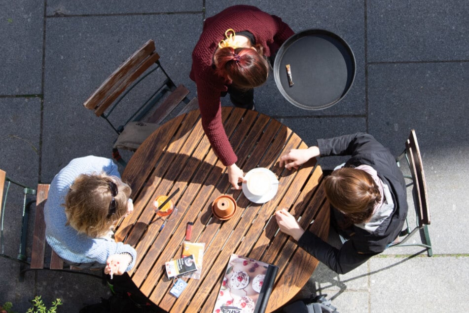 Zwei junge Frauen werden im Außenbereich eines Cafés von einer Kellnerin bedient.