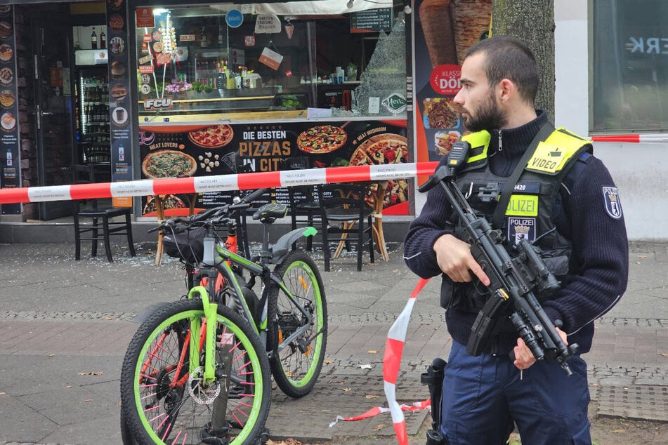 Ein schwer bewaffneter Polizist sichert den Tatort an einem Grill-Imbiss.