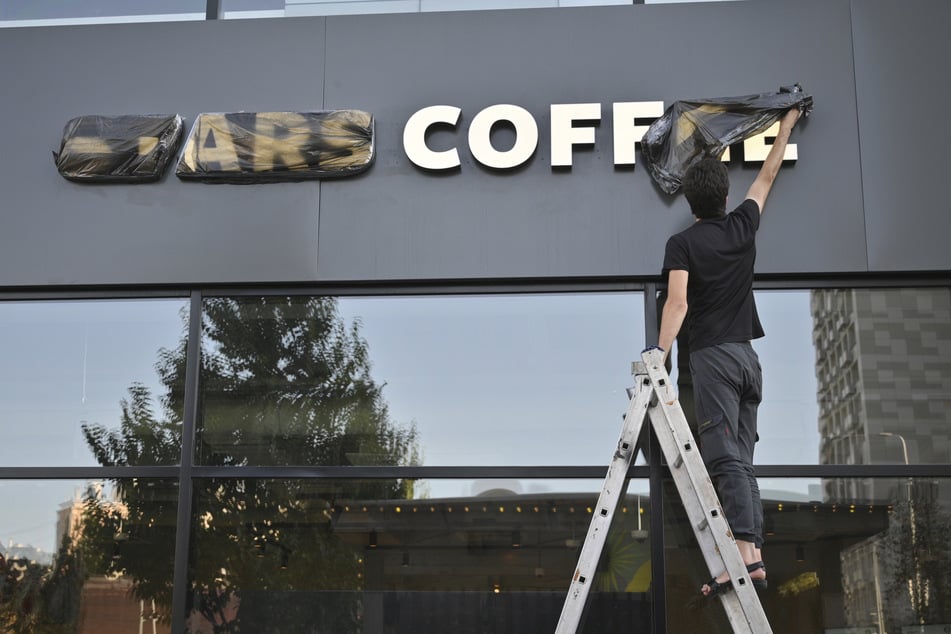 Ein Arbeiter entfernt die Abdeckung vom Schriftzug eines neu eröffneten Coffee-Shops mit dem Namen "Stars Coffee" am ehemaligen Standort eines Starbucks.
