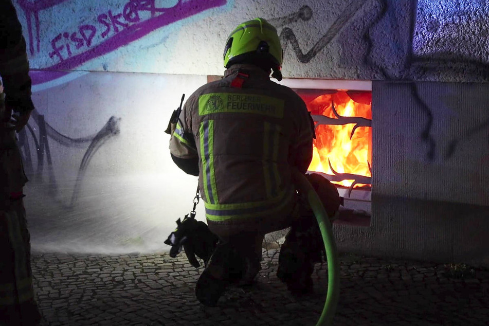 Ein Feuerwehrmann löscht den Brand in der Manteuffelstraße durch ein Kellerfenster.