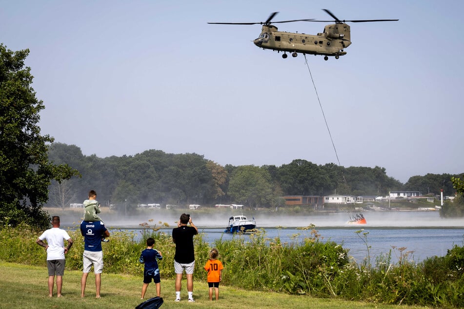 Tagesausflügler beobachten einen Chinook-Hubschrauber dabei, wie er neues Löschwasser holt.
