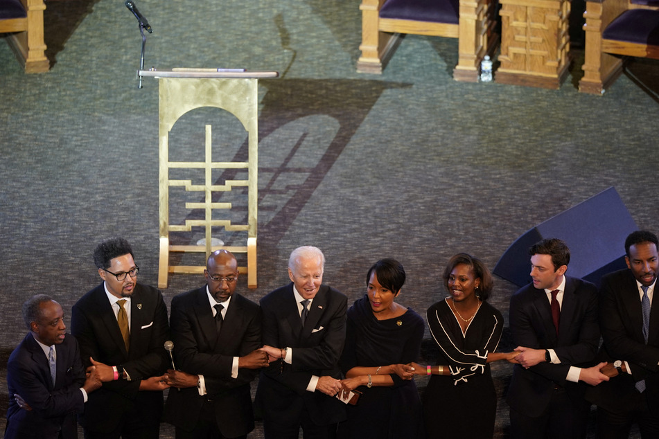 President Joe Biden stands hand in hand next to Georgia Sen. Raphael Warnock, a senior pastor at Ebenezer Baptist Church, and others ahead of the holiday honoring Martin Luther King Jr.