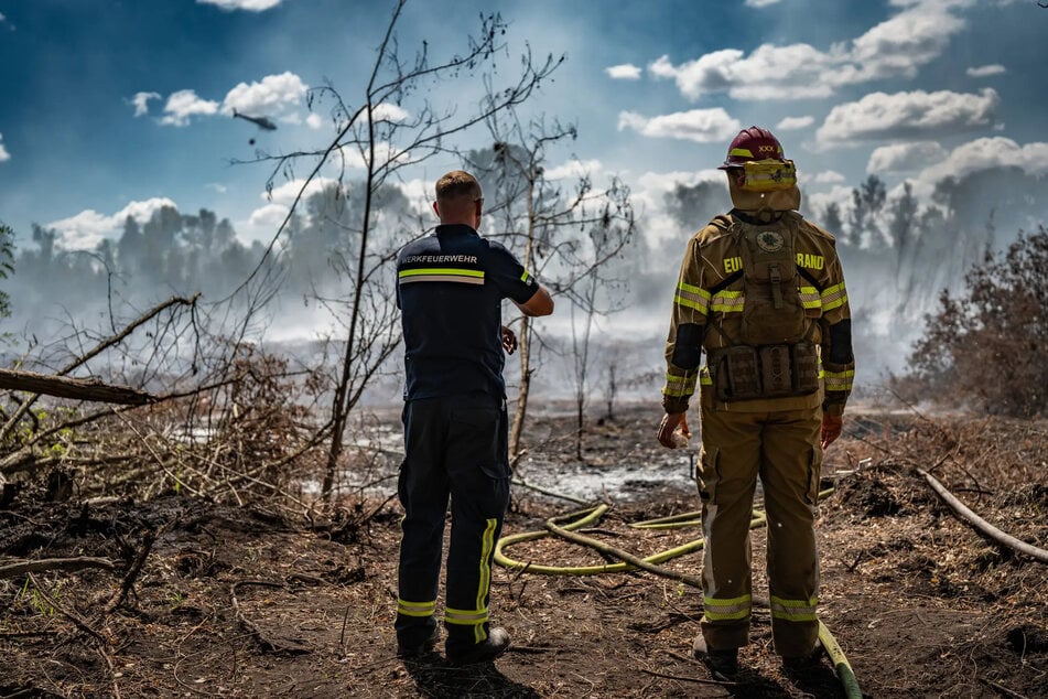 Feuerwehrleute stehen vor der qualmenden Brache, zu löschen gibt es für sie hier nichts mehr.