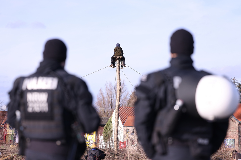 Polizisten beobachten zwei Klimaschutzaktivisten, die auf einem Monopod am Rand von Lützerath sitzen.