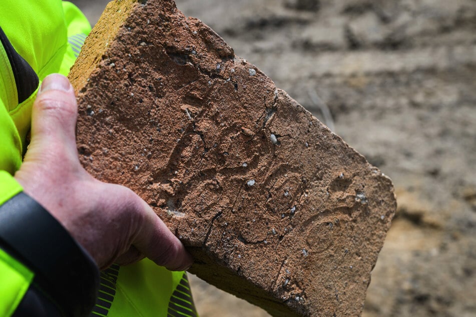 Ein Mitarbeiter vom Landesamt für Archäologie hält einen Ziegelstein aus dem Jahr 1806 in den Händen.