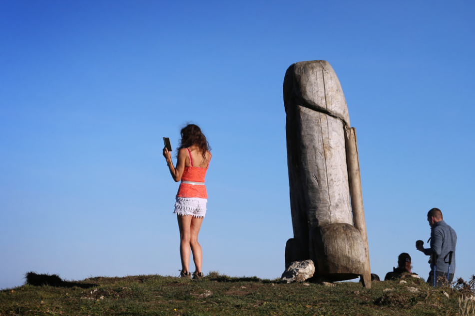 Eine Frau macht ein Selfie mit der zwei Meter hohen Penis-Skulptur aus Holz auf dem Grat des Grünten.