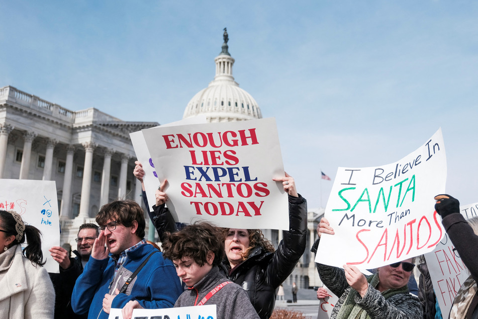 People hold signs calling for the resignation of Santos outside the US Capitol.