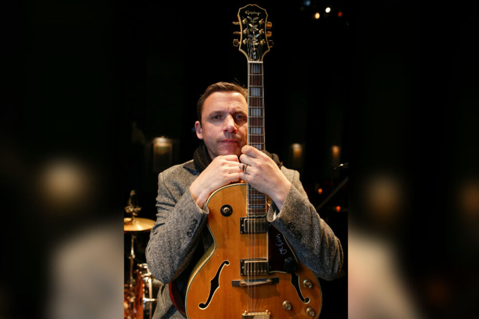 Der Musiker Rocko Schamoni sitzt mit seiner Gitarre auf einer Hamburger Kabarett-Bühne.