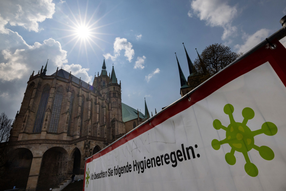 Ein großes Schild weist auf dem Erfurter Domplatz auf die Corona-Regeln hin. In Thüringen ist die Situation stabil. Vier Gebiete, darunter Erfurt, weisen inzwischen eine Inzidenz von unter 100 vor.