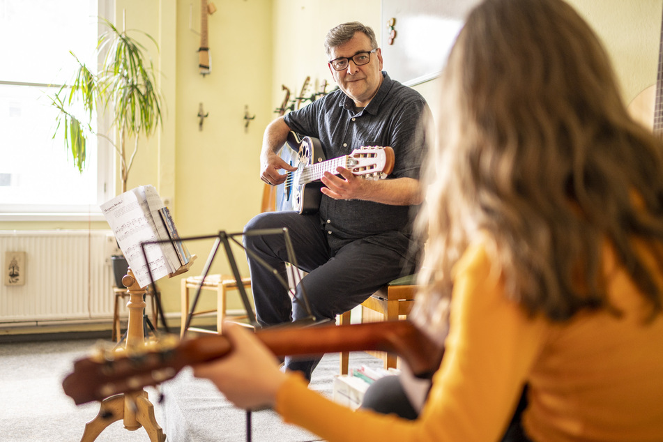 Ein Lehrer bringt in einer Musikschule seiner Schülerin das Spielen einer Gitarre bei.