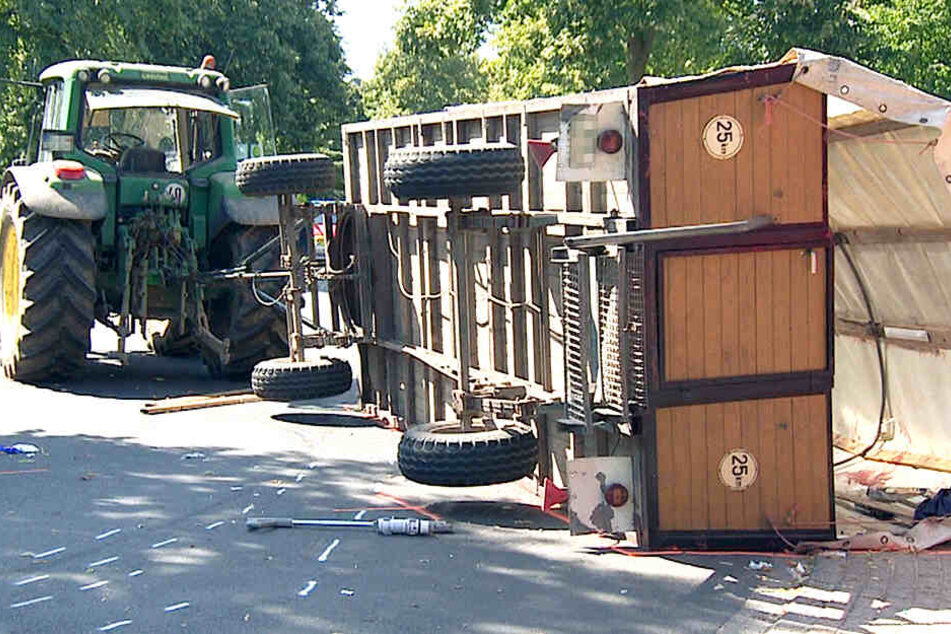 Ein Planwagen liegt umgekippt auf der Straße, hinter einem Traktor.