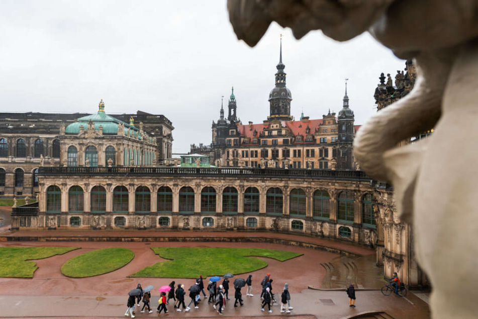 Touristen gehen bei Regen durch den Dresdner Zwinger. Im Hintergrund ist das Residenzschloss und der Hausmannsturm zu sehen.