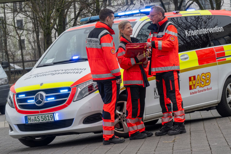 Christoph Plettner (l.-r.), Andrea Deutlmoser und Stephan Jansen vom Münchner Kriseninterventionsteam KIT-München stehen zusammen an einem Einsatzwagen.