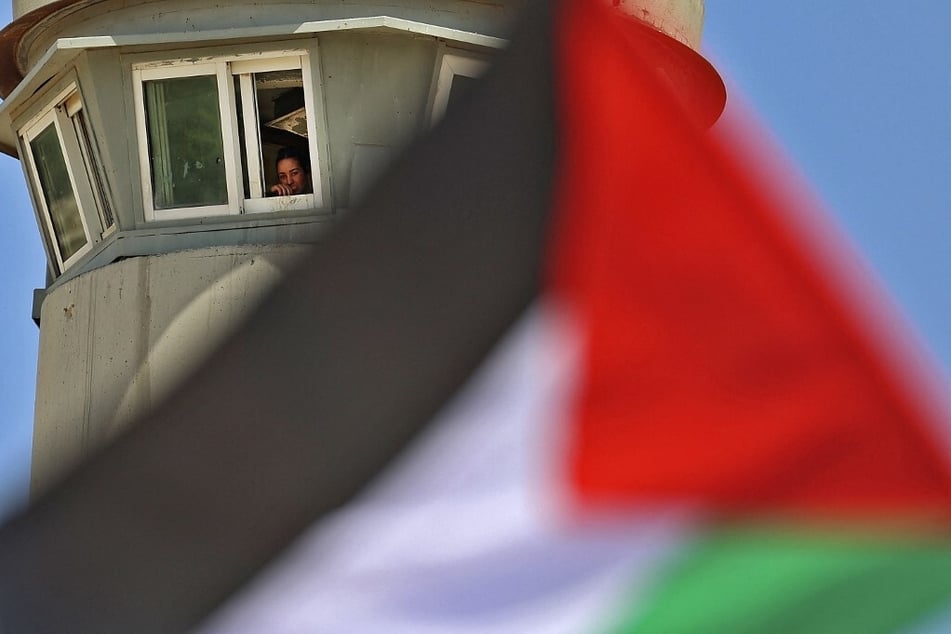 An Isreali soldier watches from a tower as Palestinian demonstrators wave the national flag in the city of Tubas during a gathering to denounce Israeli settlement expansion in the Jordan Valley.